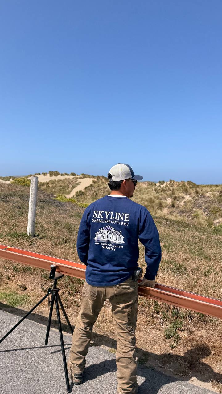 Skyline crew member in branded sweatshirt overlooking Sonoma coast dunes carrying copper gutter