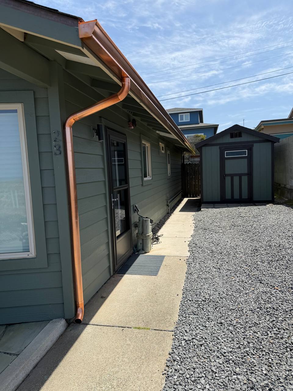 Copper gutter and downspout along a green-sided home beside a concrete walkway