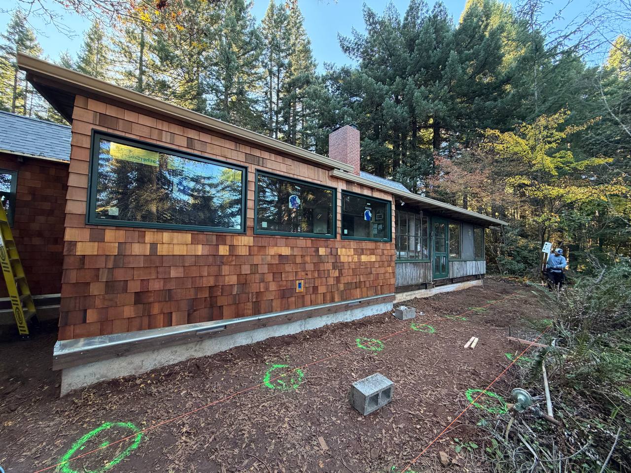 Gutter along the roofline of a wood-shingled home at a wooded job site
