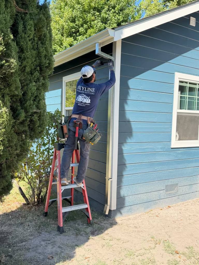 Skyline installer fitting a downspout on a blue house